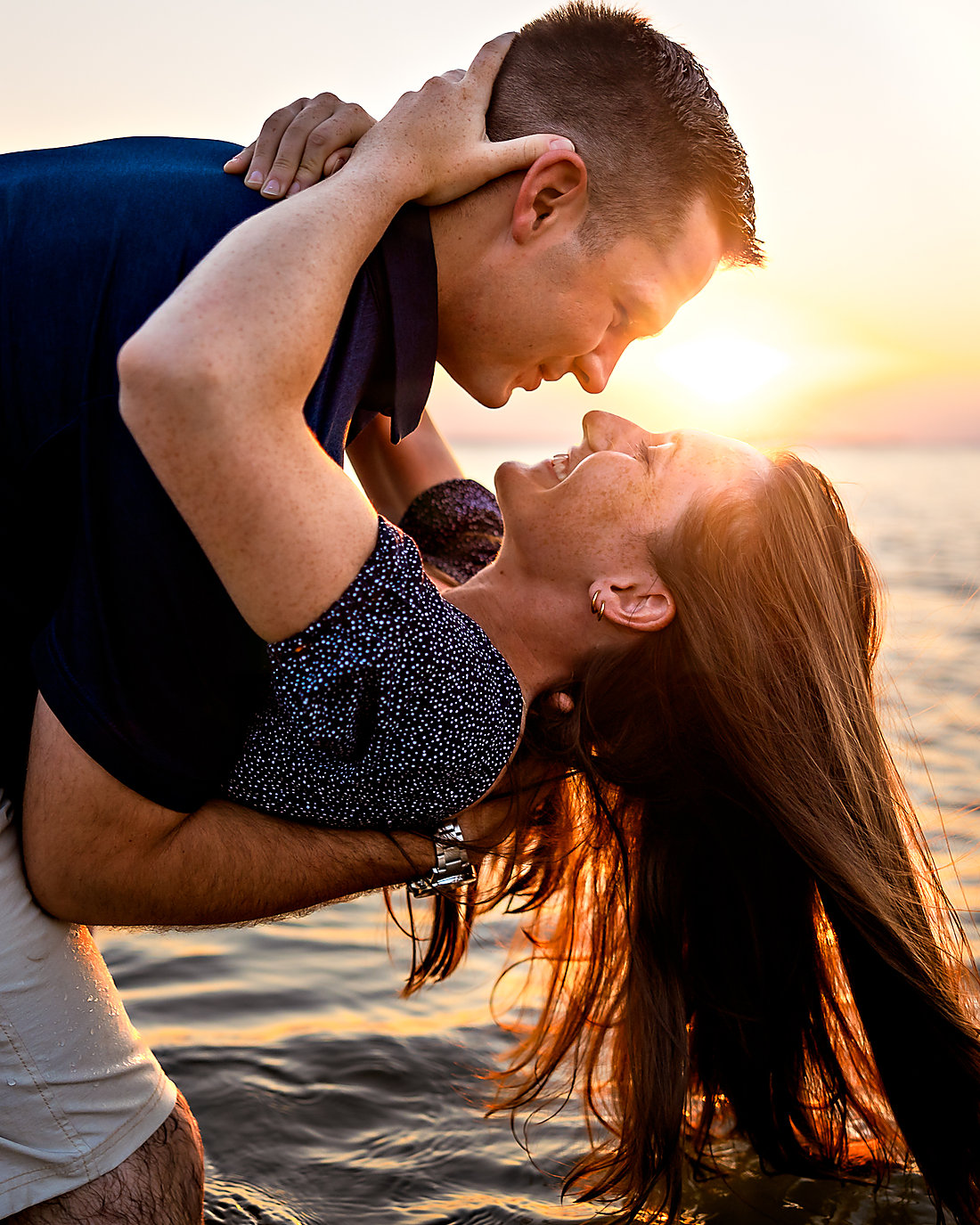 A couple at the water's edge at sunset, him dipping her back