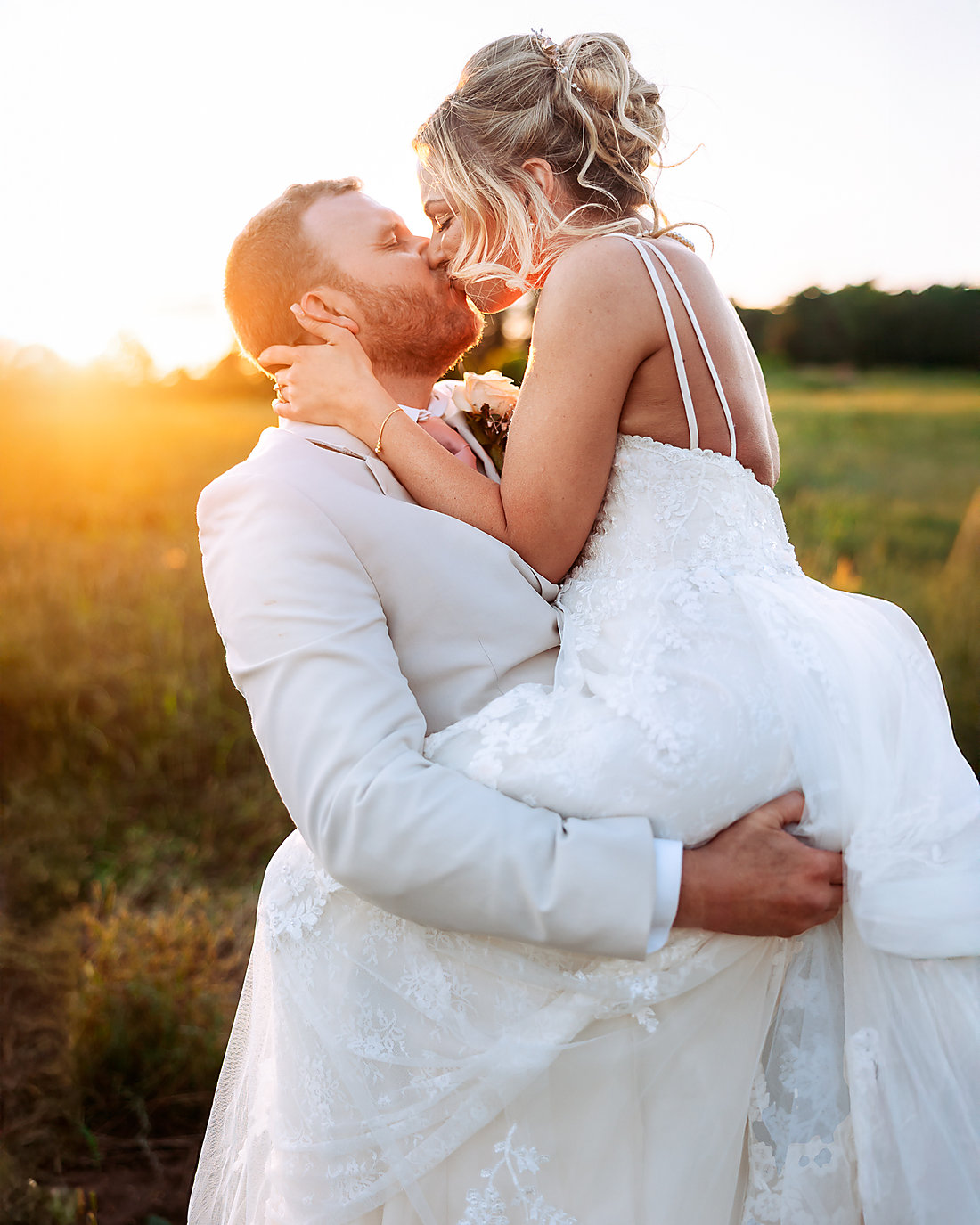 A bride and groom kissing, the sun behind them