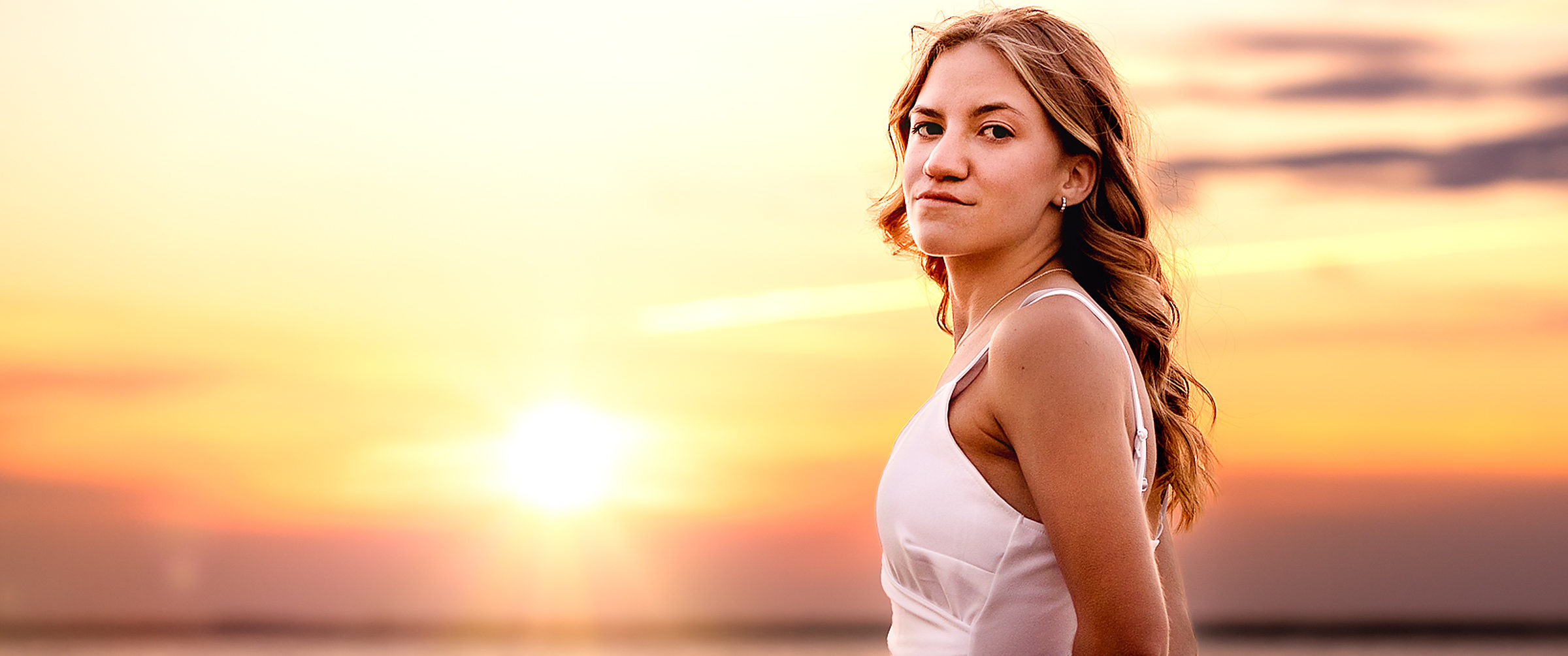 A young woman in a white dress standing in the water at sunset