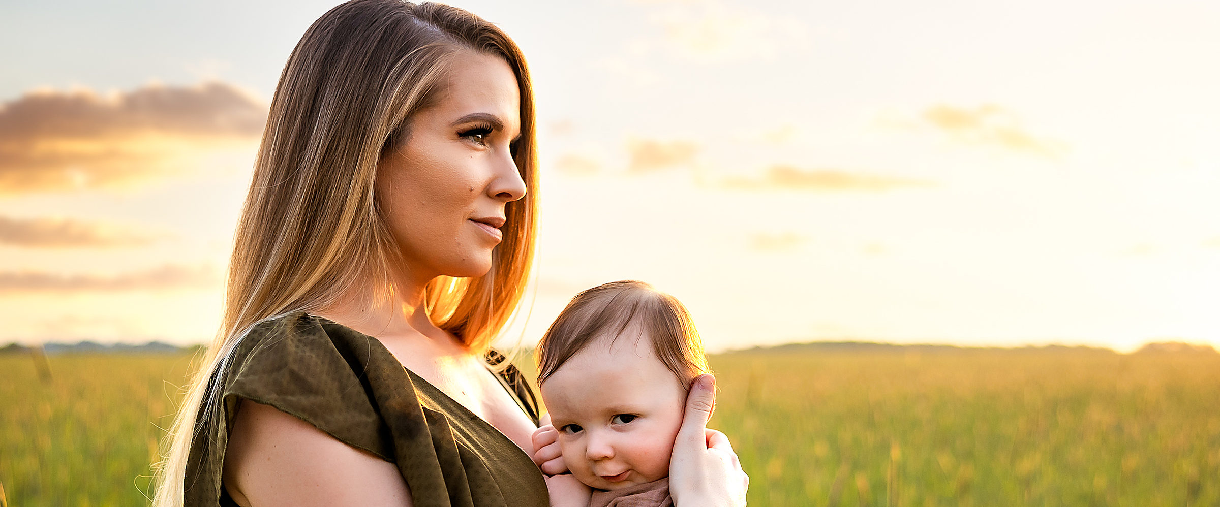 A mother holding her baby in a tall grass field at sunset