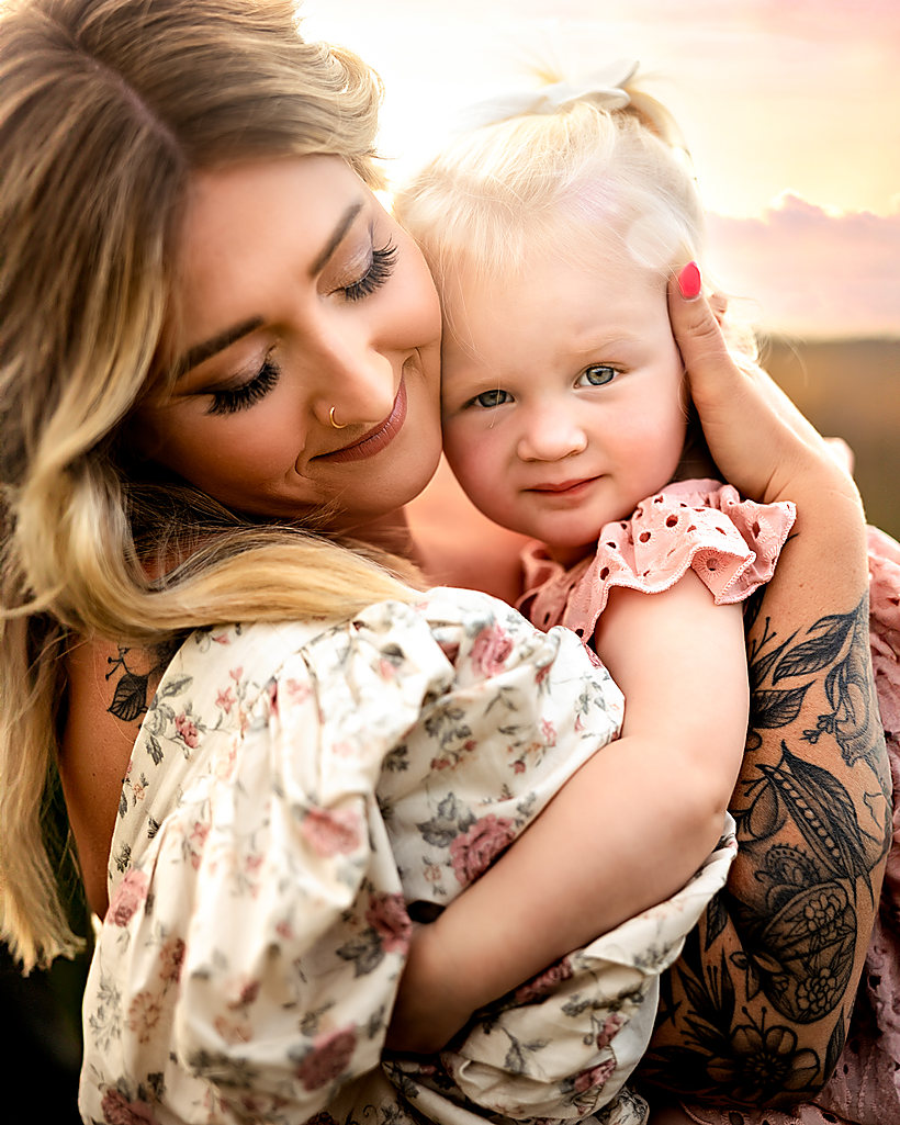 A mother holding her toddler cheek to cheek in the evening sun
