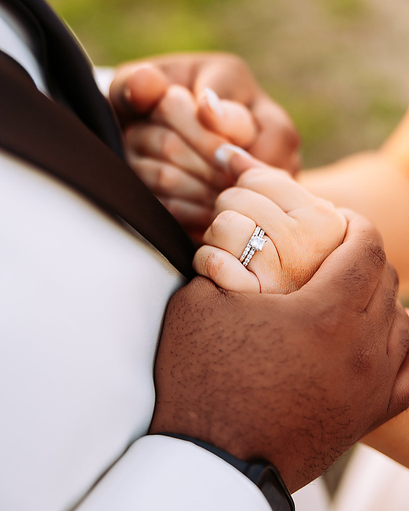 A bride and groom holding hands, her ring in the light