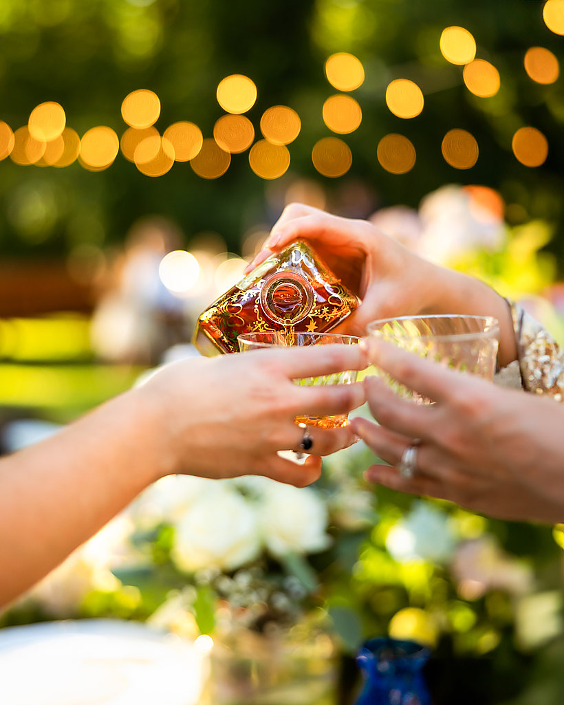 A wedding toast, glasses raised under string lights